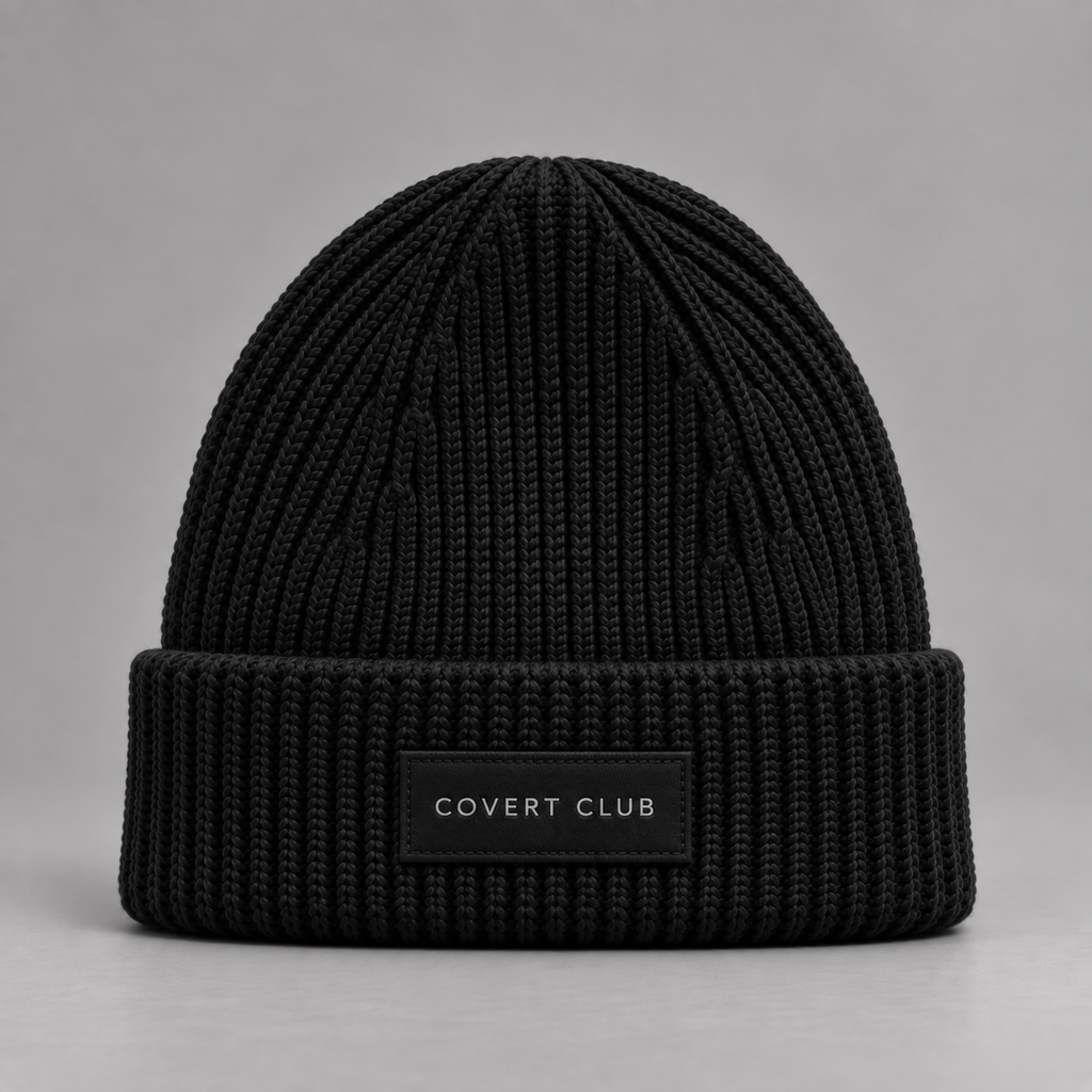 A black ribbed knit beanie hat with a folded cuff and a small black label reading 'COVERT CLUB' in white text, photographed against a neutral gray background.