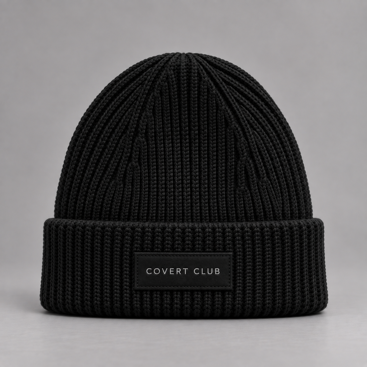 A black ribbed knit beanie hat with a folded cuff and a small black label reading 'COVERT CLUB' in white text, photographed against a neutral gray background.